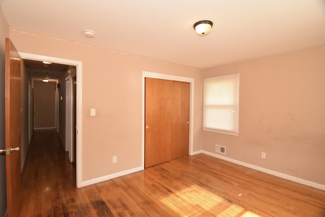 unfurnished bedroom with baseboards, visible vents, a closet, and wood finished floors