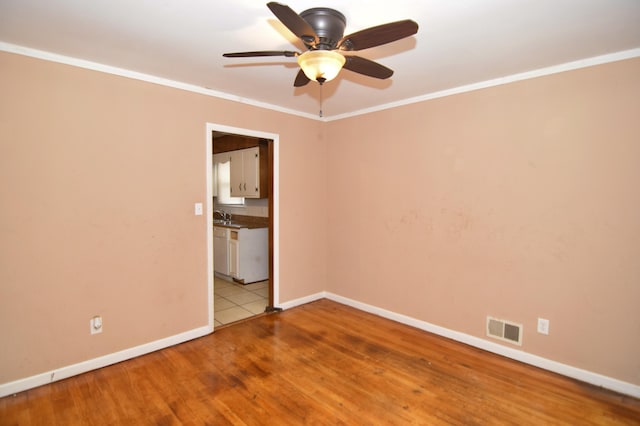 spare room with baseboards, wood finished floors, visible vents, and crown molding