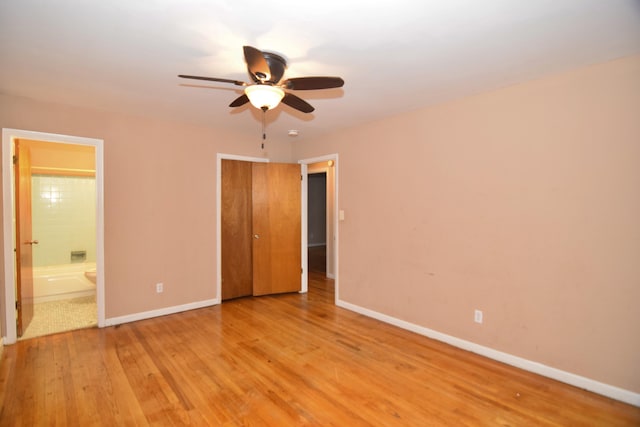 unfurnished bedroom featuring a closet, a ceiling fan, ensuite bath, light wood-type flooring, and baseboards