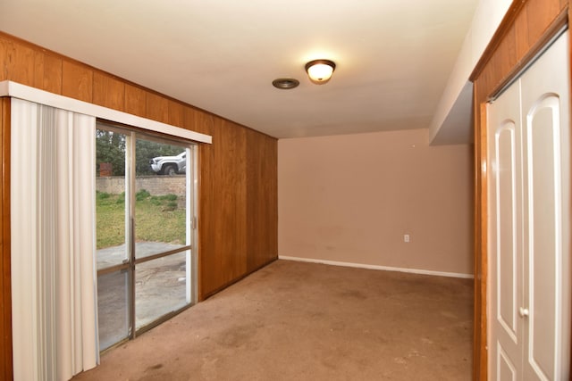 unfurnished room with light carpet, wood walls, and baseboards