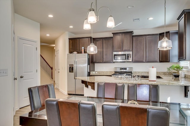 kitchen featuring a breakfast bar, light stone counters, hanging light fixtures, and stainless steel appliances