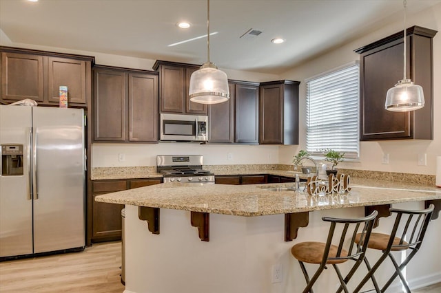 kitchen featuring light stone countertops, sink, stainless steel appliances, pendant lighting, and a breakfast bar area