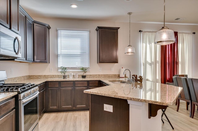 kitchen featuring dark brown cabinetry, sink, hanging light fixtures, stainless steel appliances, and a breakfast bar area