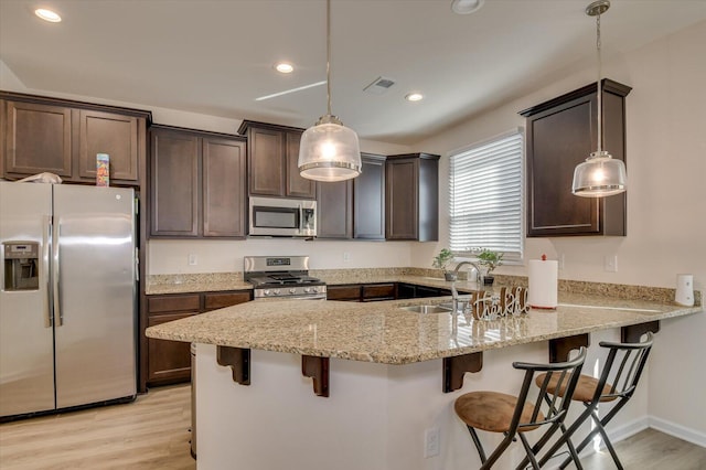 kitchen with a breakfast bar, sink, hanging light fixtures, and appliances with stainless steel finishes