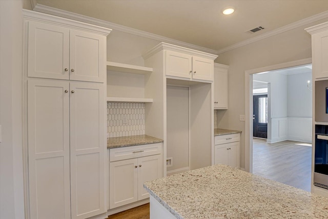 kitchen featuring white cabinetry, hardwood / wood-style flooring, ornamental molding, and light stone countertops