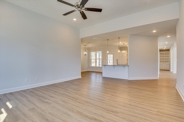 unfurnished living room featuring sink, ceiling fan with notable chandelier, and light hardwood / wood-style flooring