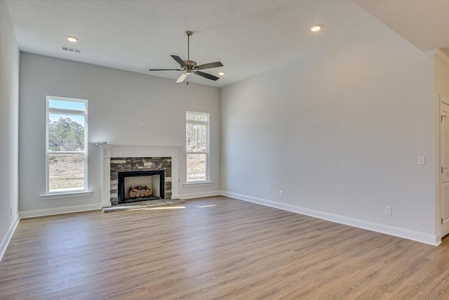 unfurnished living room with ceiling fan, a stone fireplace, and light hardwood / wood-style floors