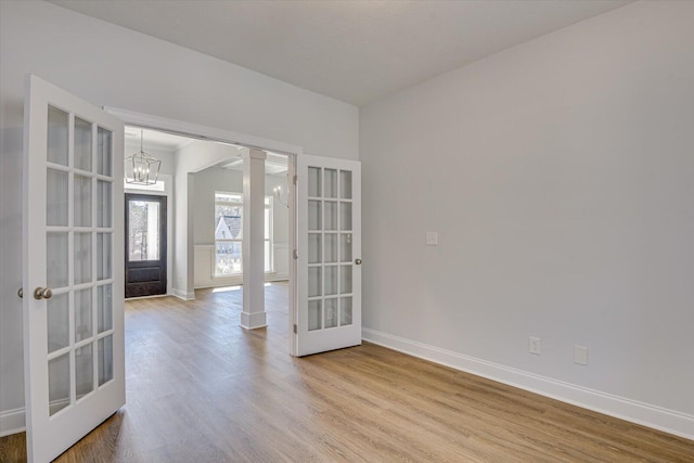 spare room featuring decorative columns, a chandelier, light wood-type flooring, and french doors