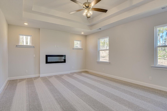 unfurnished living room with ceiling fan, light colored carpet, and a tray ceiling