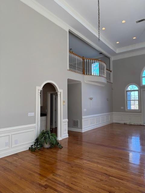 unfurnished living room with a tray ceiling, crown molding, wood-type flooring, and a high ceiling