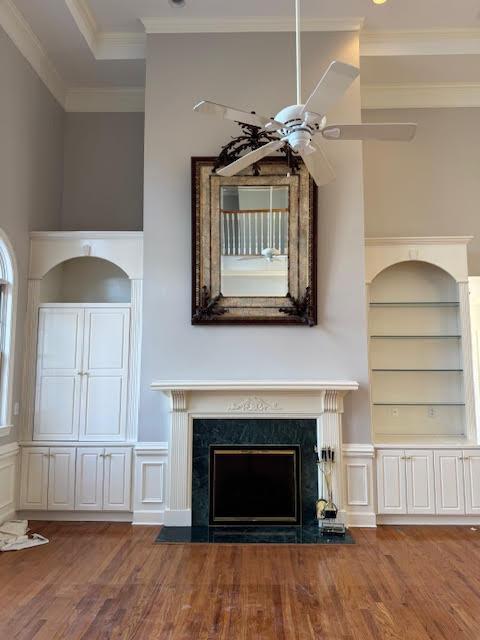 unfurnished living room featuring hardwood / wood-style floors, ceiling fan, a high end fireplace, crown molding, and built in shelves