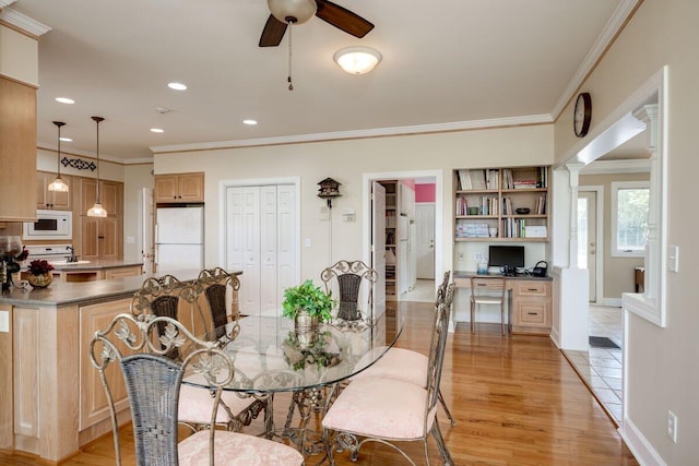 dining room featuring ceiling fan, ornamental molding, built in desk, and light wood-type flooring