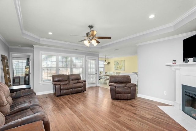 living area with wood finished floors, baseboards, a tray ceiling, a fireplace with flush hearth, and crown molding