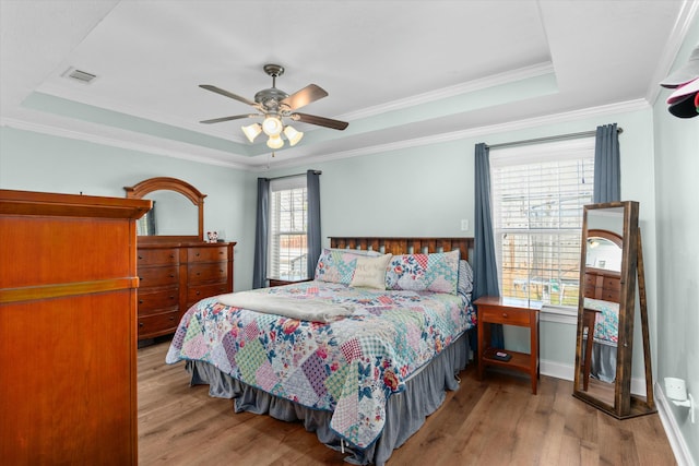 bedroom with a tray ceiling, crown molding, wood finished floors, and visible vents