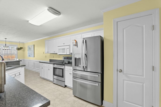 kitchen with stainless steel appliances, dark countertops, ornamental molding, and white cabinetry