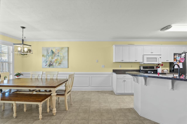 kitchen with white microwave, stainless steel electric range, freestanding refrigerator, white cabinets, and a kitchen breakfast bar