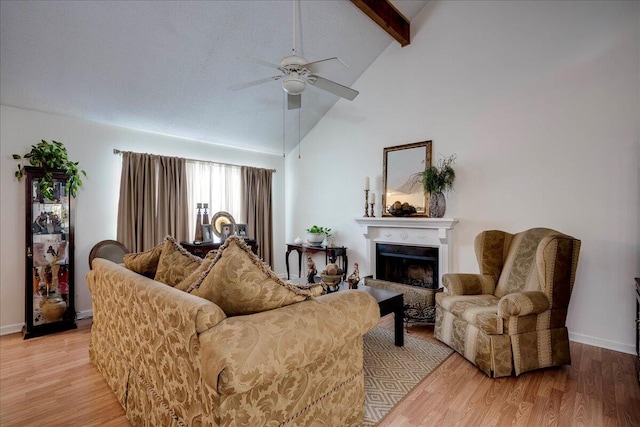 living area with ceiling fan, a fireplace with raised hearth, light wood-style floors, beamed ceiling, and high vaulted ceiling