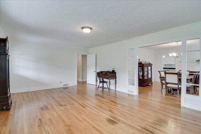 living room with french doors, light wood-type flooring, a textured ceiling, and an inviting chandelier