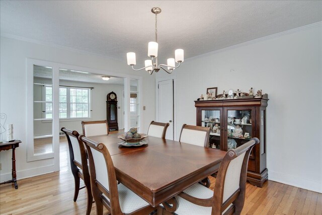 dining room featuring a textured ceiling, crown molding, light hardwood / wood-style flooring, and an inviting chandelier