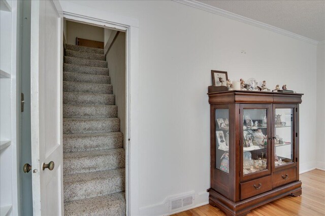 stairs with hardwood / wood-style floors, ornamental molding, and a textured ceiling