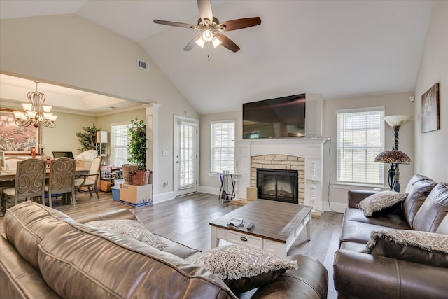 living room featuring visible vents, plenty of natural light, a stone fireplace, and ceiling fan with notable chandelier