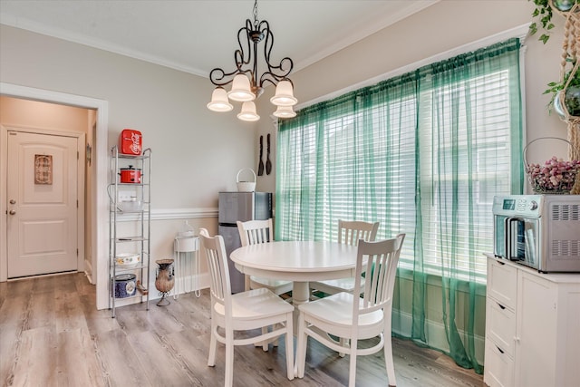 dining space with a toaster, ornamental molding, a notable chandelier, and light wood-style floors