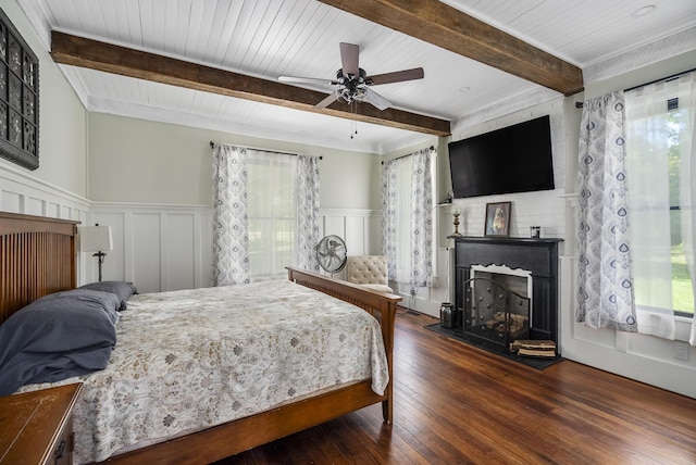 bedroom featuring a large fireplace, ceiling fan, beam ceiling, and dark hardwood / wood-style flooring