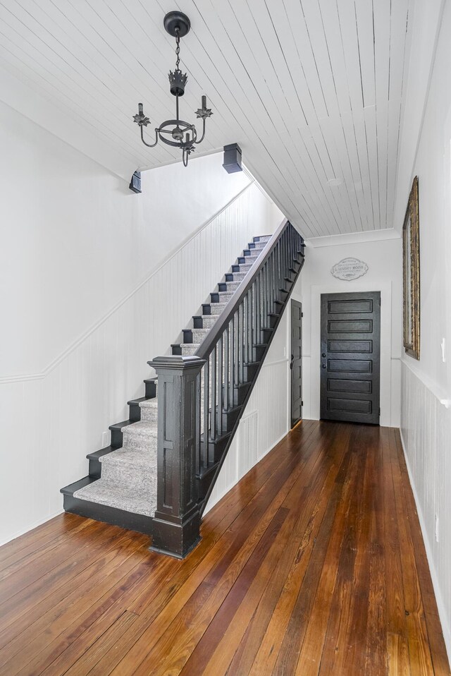 stairs with hardwood / wood-style floors, a notable chandelier, wooden ceiling, and crown molding