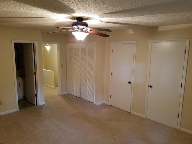 unfurnished bedroom with multiple closets, light colored carpet, ensuite bath, and ceiling fan