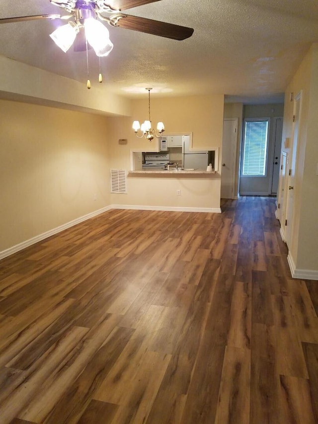 unfurnished living room featuring ceiling fan with notable chandelier, dark wood-type flooring, and a textured ceiling