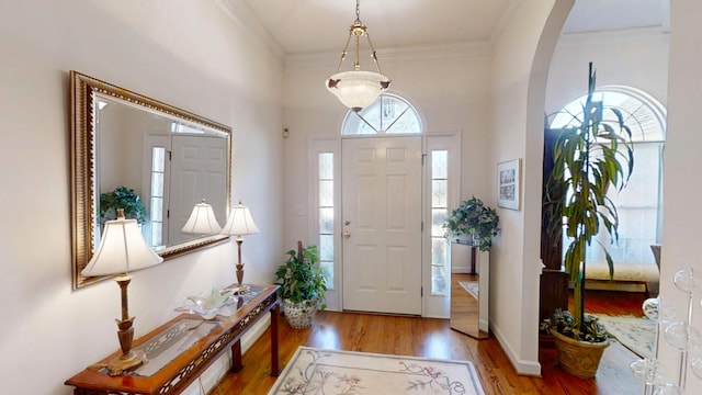 foyer featuring baseboards, wood finished floors, arched walkways, and ornamental molding