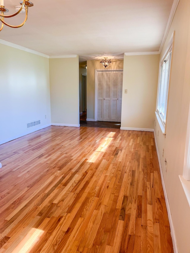 empty room featuring visible vents, an inviting chandelier, light wood-style floors, ornamental molding, and baseboards