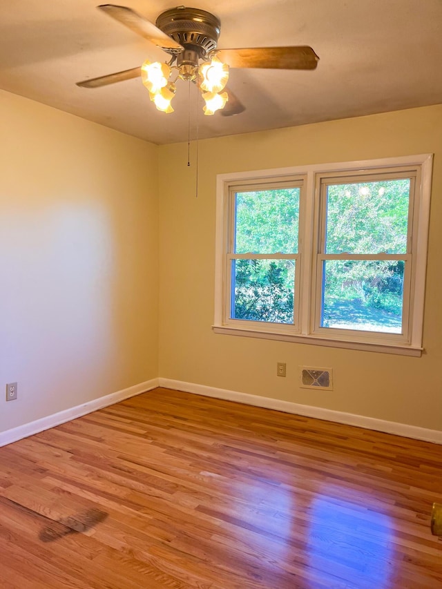 unfurnished room with a wealth of natural light, wood finished floors, visible vents, and baseboards