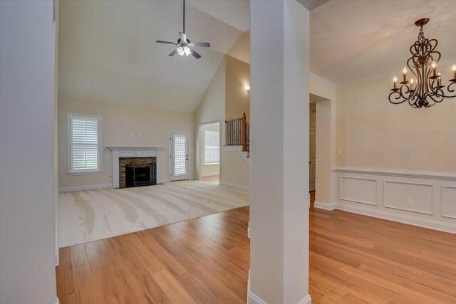 unfurnished living room with ceiling fan with notable chandelier, a fireplace, high vaulted ceiling, and light hardwood / wood-style flooring