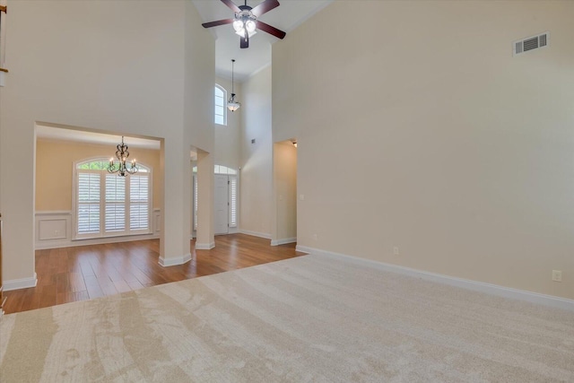 unfurnished living room featuring a high ceiling, ceiling fan with notable chandelier, crown molding, and a healthy amount of sunlight