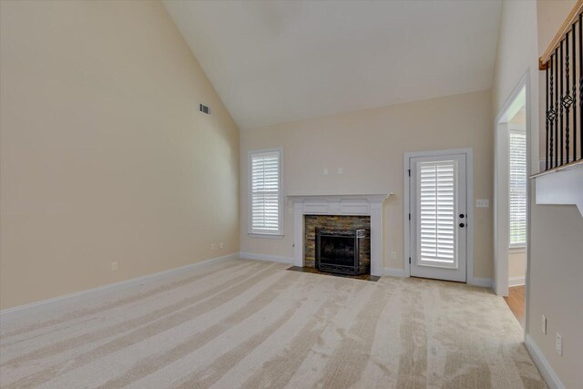 unfurnished living room featuring high vaulted ceiling, a stone fireplace, a wealth of natural light, and light colored carpet