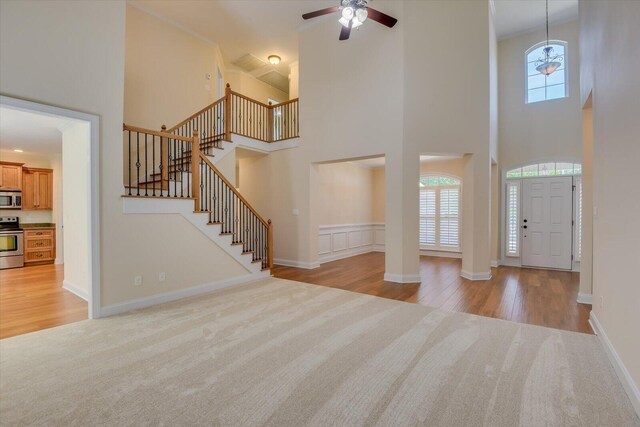 foyer featuring ornate columns, ceiling fan, a high ceiling, light colored carpet, and ornamental molding