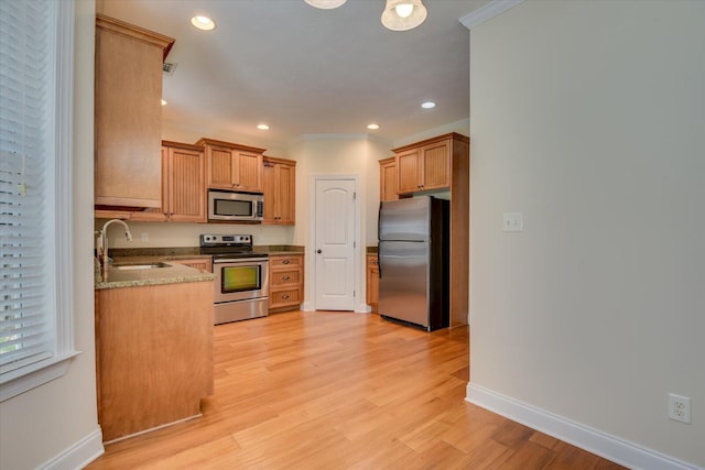 kitchen with light stone countertops, sink, light wood-type flooring, appliances with stainless steel finishes, and ornamental molding