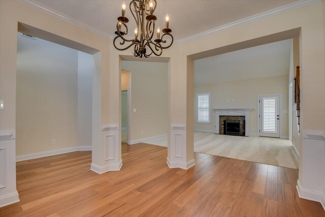 unfurnished living room featuring decorative columns, crown molding, a chandelier, a fireplace, and light hardwood / wood-style floors