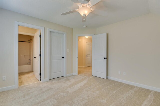 unfurnished bedroom with a closet, light colored carpet, ceiling fan, and ensuite bathroom