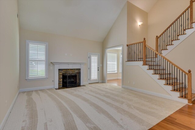 unfurnished living room with a fireplace, high vaulted ceiling, and light wood-type flooring