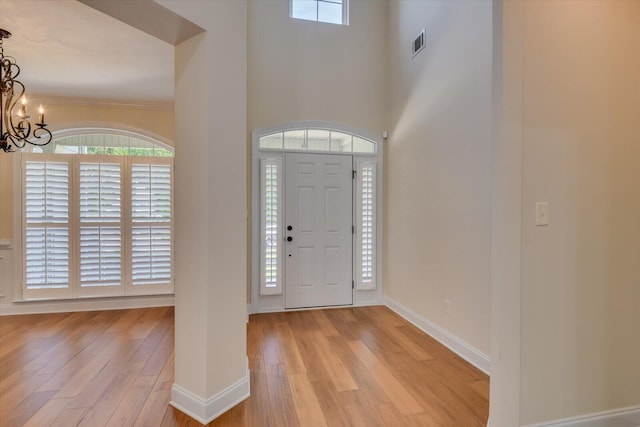 foyer entrance with a notable chandelier, light wood-type flooring, and crown molding