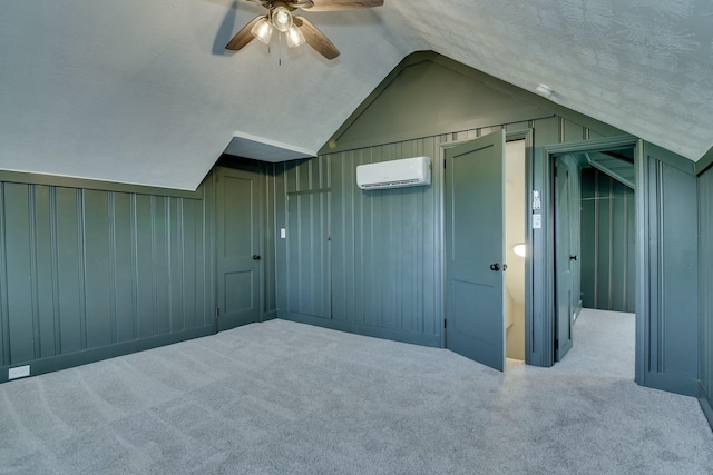 additional living space with a wall mounted air conditioner, vaulted ceiling, a textured ceiling, ceiling fan, and carpet