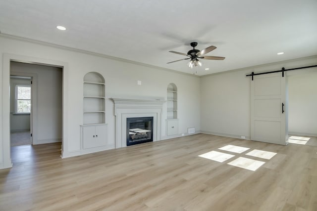 unfurnished living room featuring ceiling fan, a barn door, and light hardwood / wood-style floors