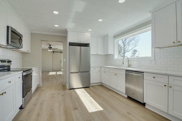 kitchen featuring crown molding, appliances with stainless steel finishes, light hardwood / wood-style floors, white cabinets, and decorative backsplash