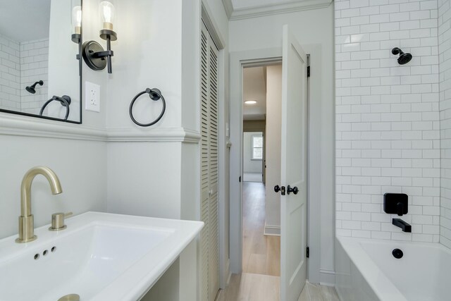 bathroom featuring sink, wood-type flooring, ornamental molding, and tiled shower / bath