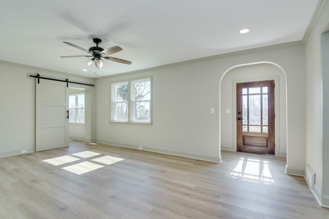 entryway featuring ceiling fan, ornamental molding, a barn door, and light hardwood / wood-style floors