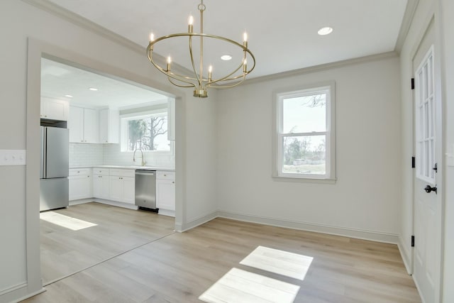 unfurnished dining area featuring ornamental molding, light hardwood / wood-style floors, sink, and a notable chandelier