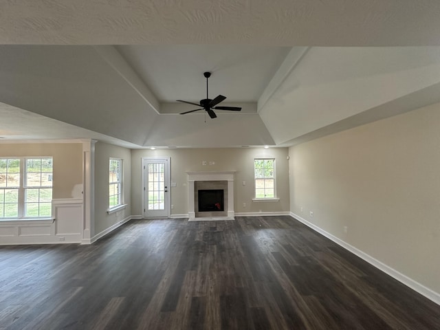 unfurnished living room featuring a raised ceiling, ceiling fan, a healthy amount of sunlight, and dark hardwood / wood-style floors