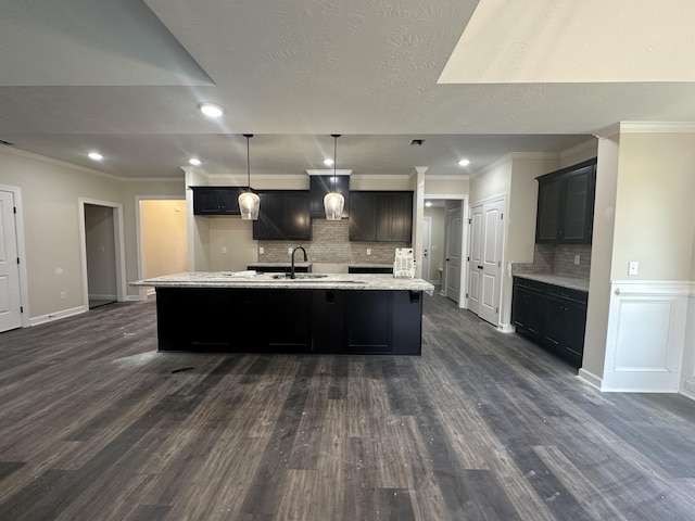 kitchen featuring backsplash, dark wood-type flooring, an island with sink, and pendant lighting